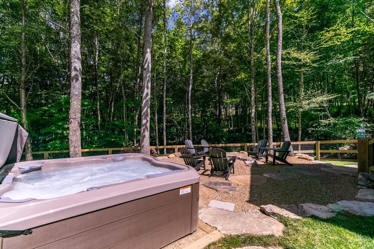 A serene exterior with a steaming hot tub and a comfortable seating area, set against a wooded backdrop. The area invites stargazing, casual conversations, and relaxation after a day of adventure.