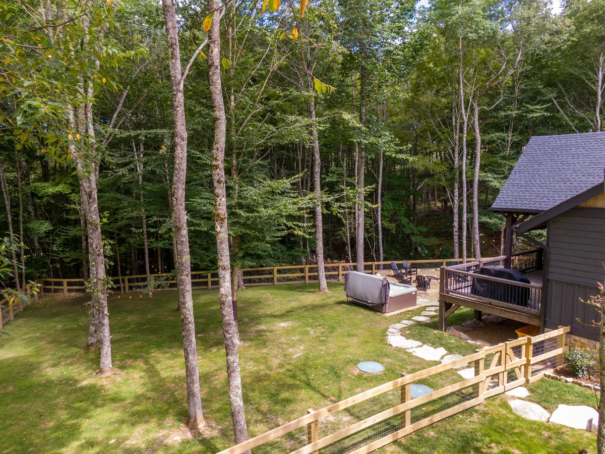 This exterior image showcases a fenced backyard area with a hot tub, patio furniture, and lush surrounding trees. The wooden fence suggests a secure outdoor space, ideal for letting dogs play off-leash. The hot tub and patio offer comfortable spots for relaxation after outdoor adventures.