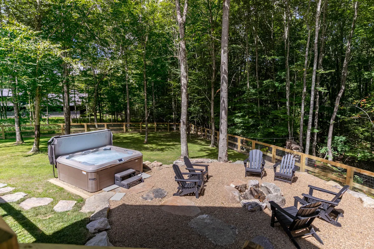 A peaceful outdoor scene featuring a private hot tub, a fire pit surrounded by Adirondack chairs, and a lush wooded backdrop. The setting feels tranquil and inviting, ideal for relaxing after a day of adventure.