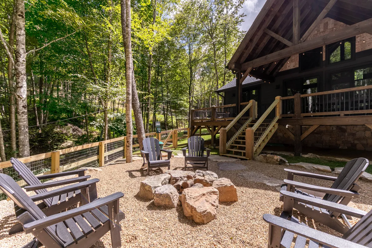 An inviting exterior scene with a glowing fire pit surrounded by Adirondack chairs, set in a forest clearing near the house. The setup is perfect for campfire gatherings, storytelling, and quiet moments in nature.