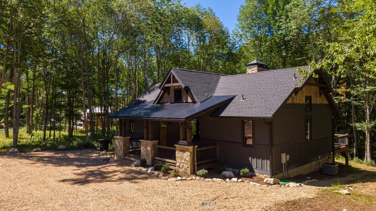 An exterior view of the stylish cabin with stone pillars, surrounded by trees and a gravel driveway. The scene conveys the welcoming character of the home as a comfortable launching point for resort adventures.